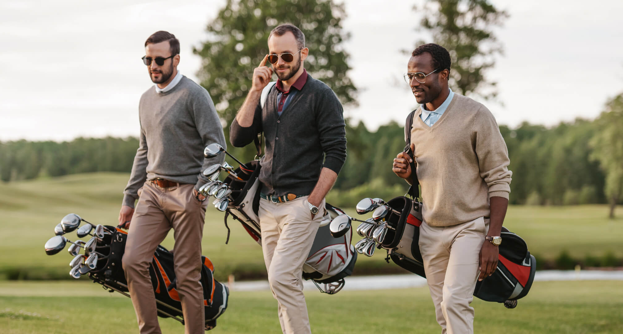 трима души, играещи голф със слънчеви очила и чанти за голф